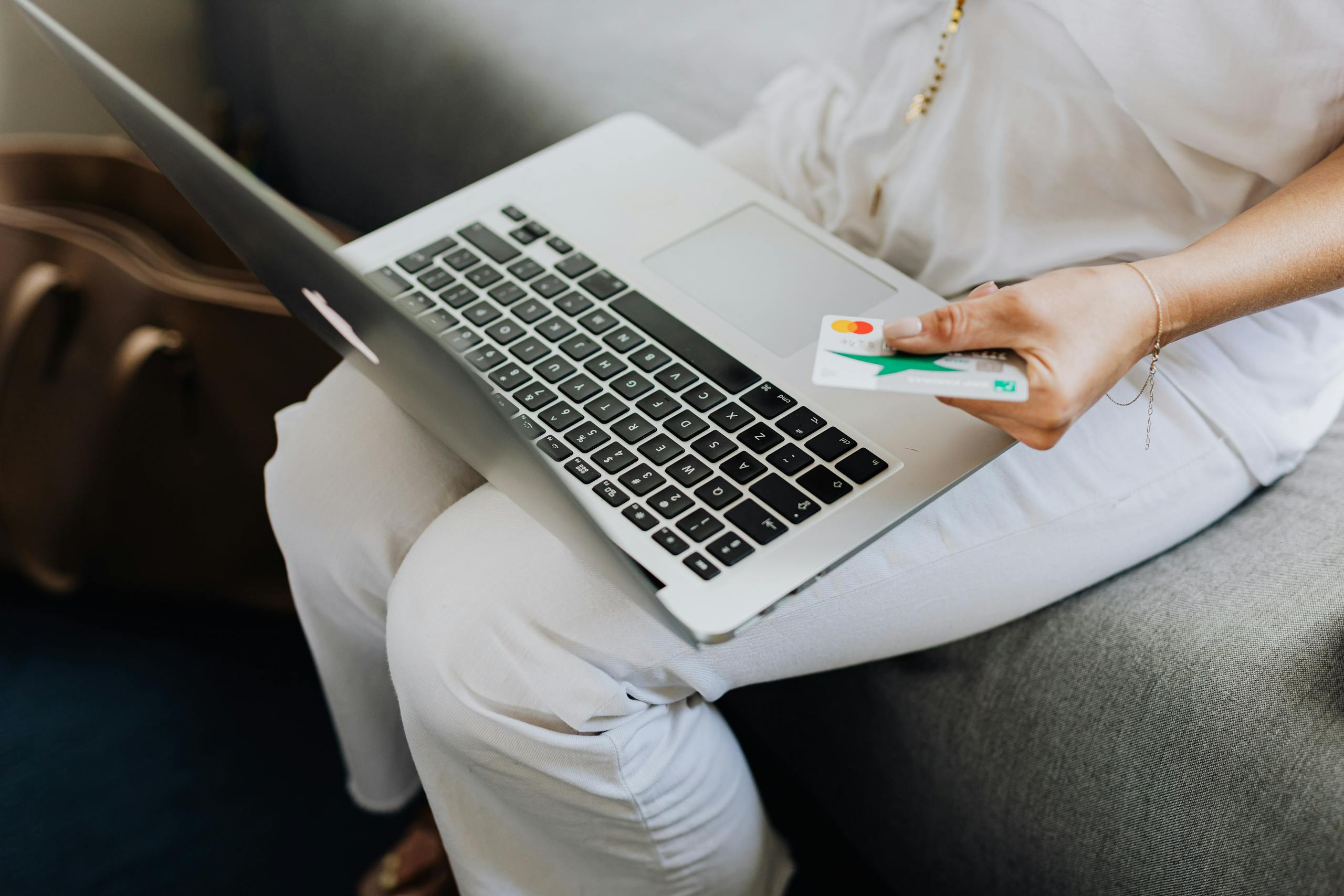 Adult using laptop and holding bank card for online shopping indoors.
